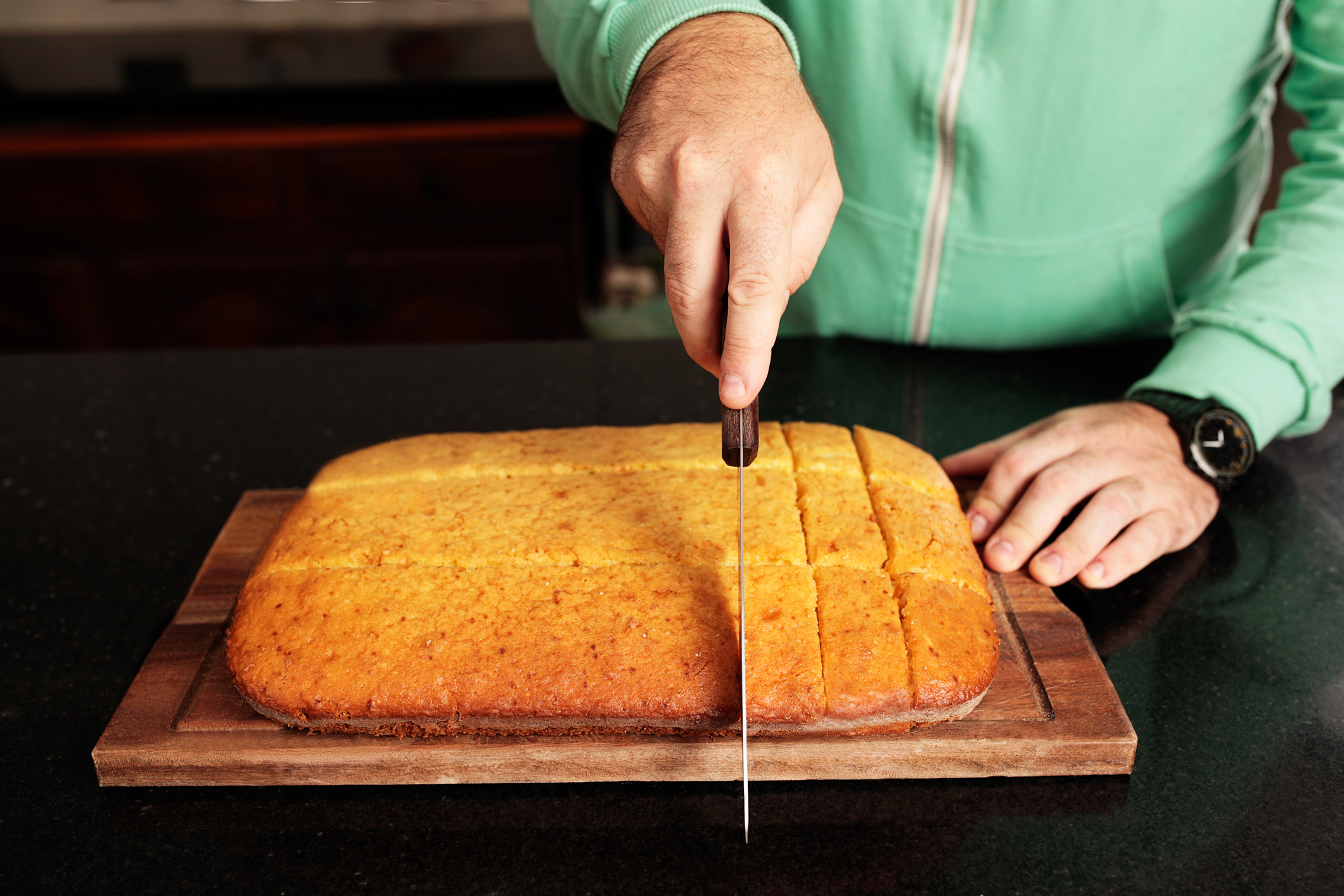 A close-up detail shot of man's hands cutting a sweet cake into portions.