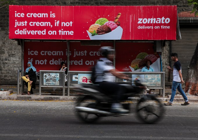 A man is riding a bike past a bus stop with an advertisement of Zomato, an Indian food-delivery company, in Mumbai, India, on June 9th, 2023.