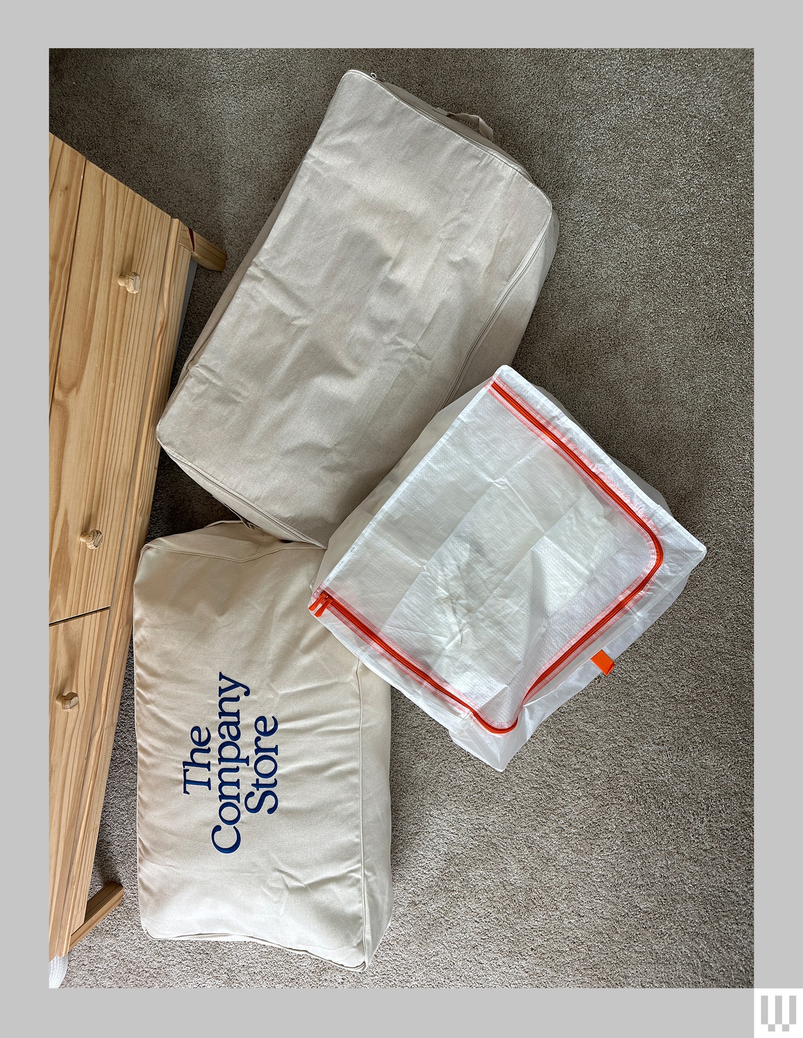 3 closed bags if various materials on the floor beside a nightstand each holding folded bed sheets