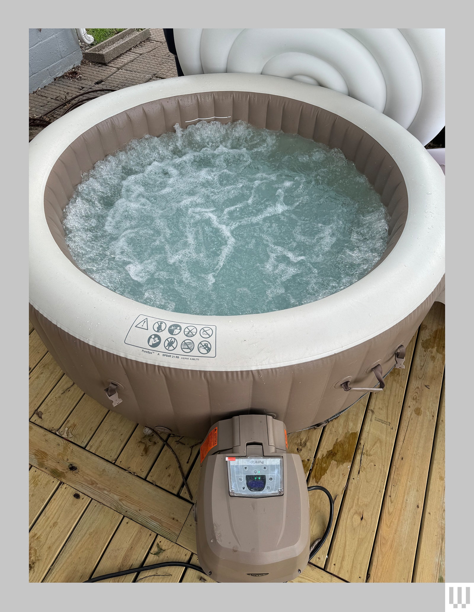 Overhead view of beige and white inflatable container with bubbling water and a small motor attached all sitting on a...