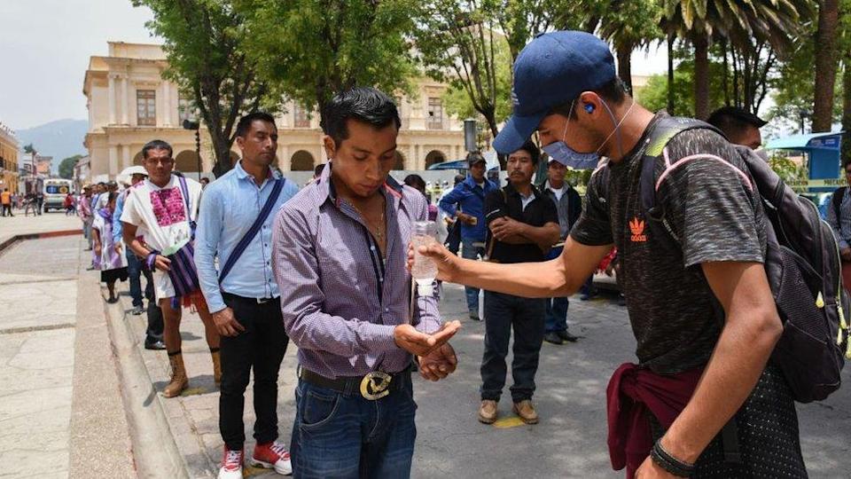 A worker sanitises people's hands as they queue for an allowance from the local government