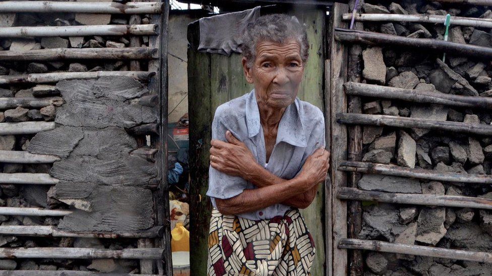 A shivering woman stands outside her damaged home