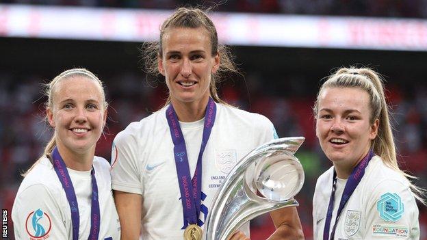 Jill Scott holding the Euro 2022 trophy with England team-mates Beth Mead and Lauren Hemp