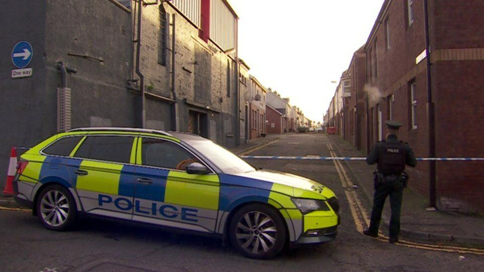 A police officer stands beside a police car parked at a cordon at Dundela Street, where Kieran Smithson and the pipe bomb were found