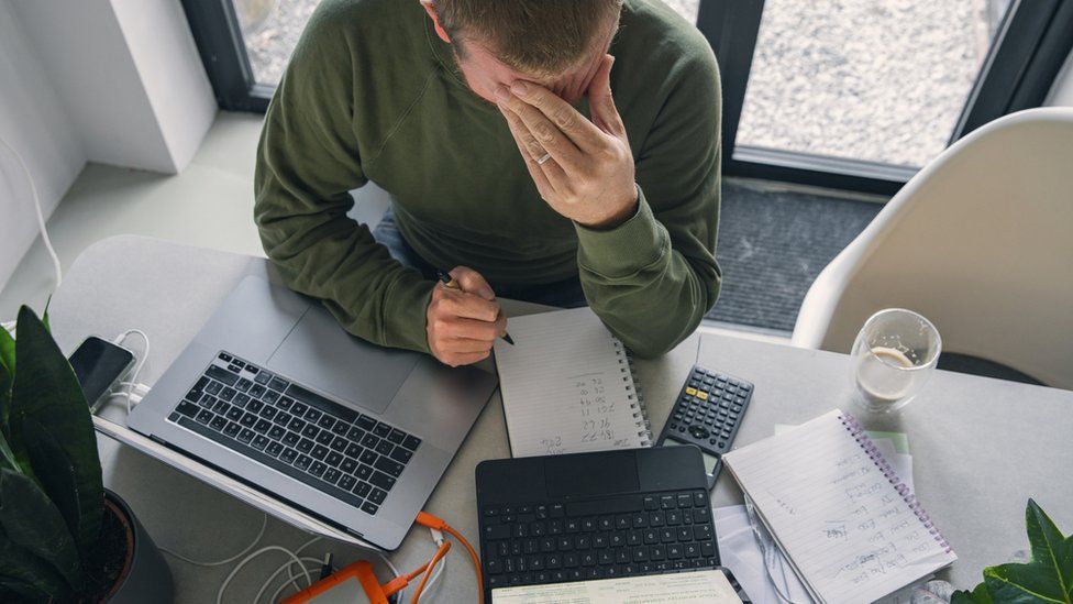 A man is seen with his head in his hand while going through his bills at a table