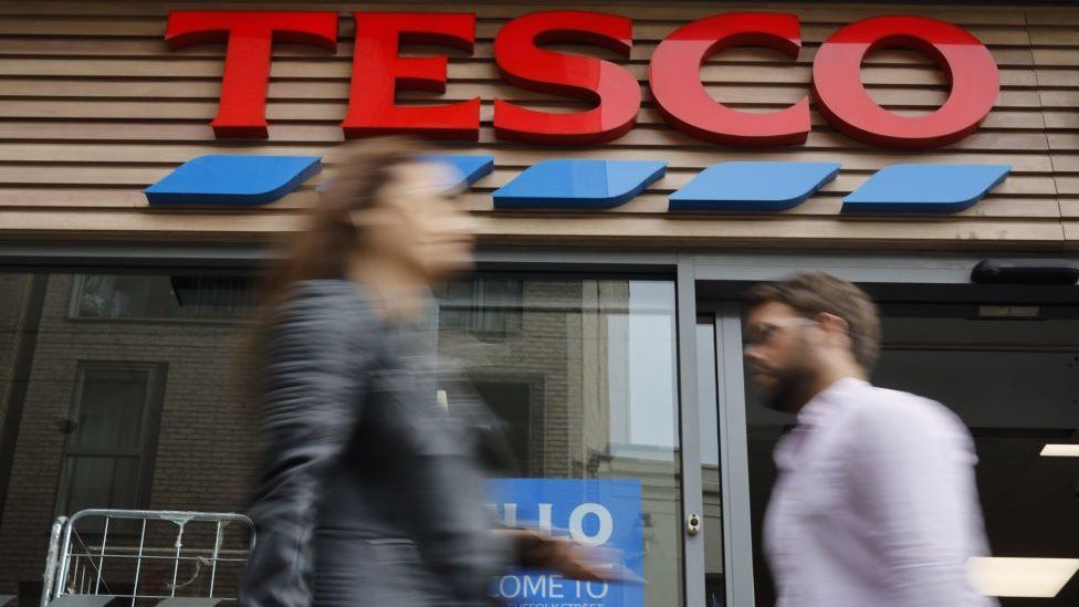 Two people walk past a Tesco store