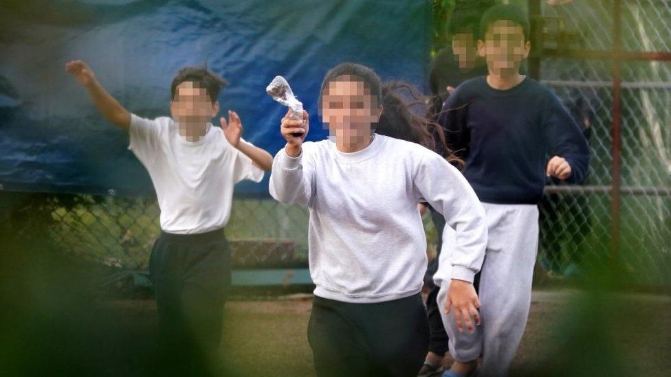 A young girl runs towards the fence carrying a message in a bottle describing conditions inside the Manston immigration short-term holding facility located at the former Defence Fire Training and Development Centre in Thanet, Kent