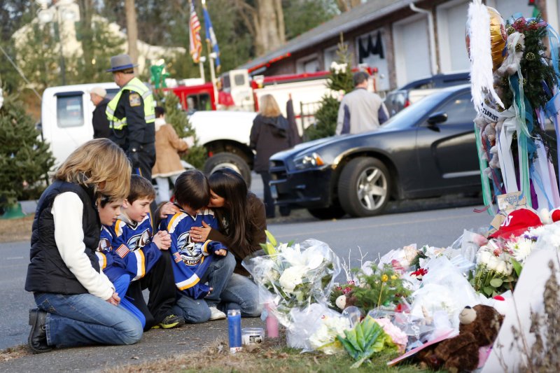 Mourners gather near a memorial filled with flowers, stuffed toys and candles at the entrance to Sandy Hook Elementary School in Newtown, Conn., following a shooting December 14, 2012. File Photo by John Angelillo/UPI | <a href="/News_Photos/lp/00684402ecb2e2e0f0064e53d7e0af84/" target="_blank">License Photo</a>