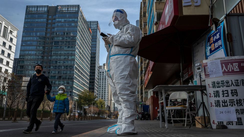 An epidemic control worker in a protective suit guards the entrance to a locked-down apartment block in Beijing