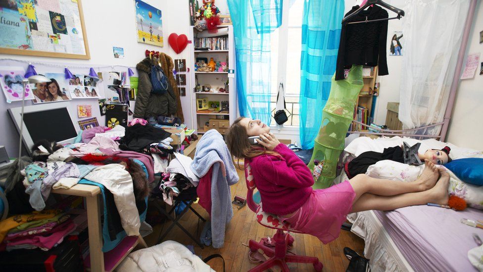 A woman sitting on her phone in a messy room.