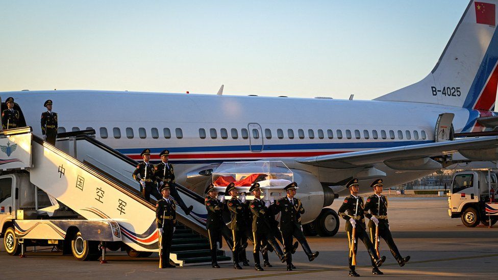 Chinese soldiers frogmarch as they carry Jiang Zemin's glass coffin off a place arriving from Shanghai