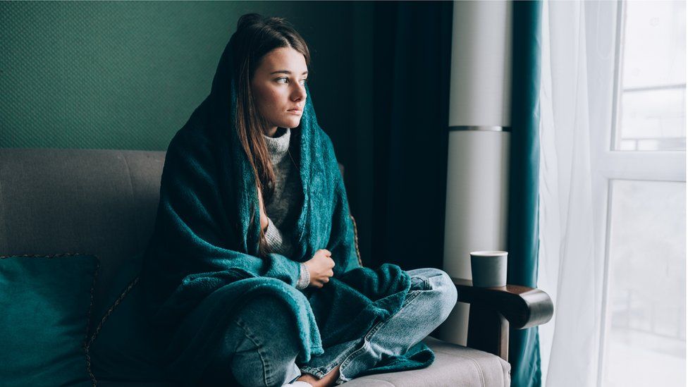 Young woman wrapped in a blanket in a cold house