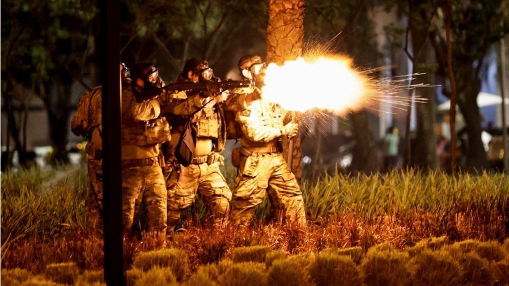 A police officer fires a shotgun as supporters of Brazil's President Jair Bolsonaro protest after supreme court justice Alexandre de Moraes ordered a temporary arrest warrant of indigenous leader Jose Acacio Serere Xavante for alleged anti-democratic acts, in Brasilia, Brazil, December 12, 2022.