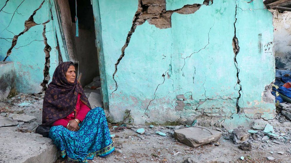 A woman sits beside a cracked wall of her house at Joshimath in Chamoli district of India's Uttarakhand state on January 10, 2023.