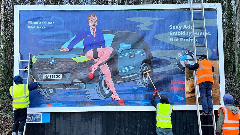 Three people putting up a spoof BMW billboard