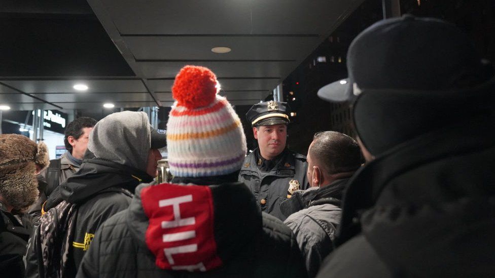 A police officer talks to migrants outside the Watson Hotel in New York City on 29 January, 2023