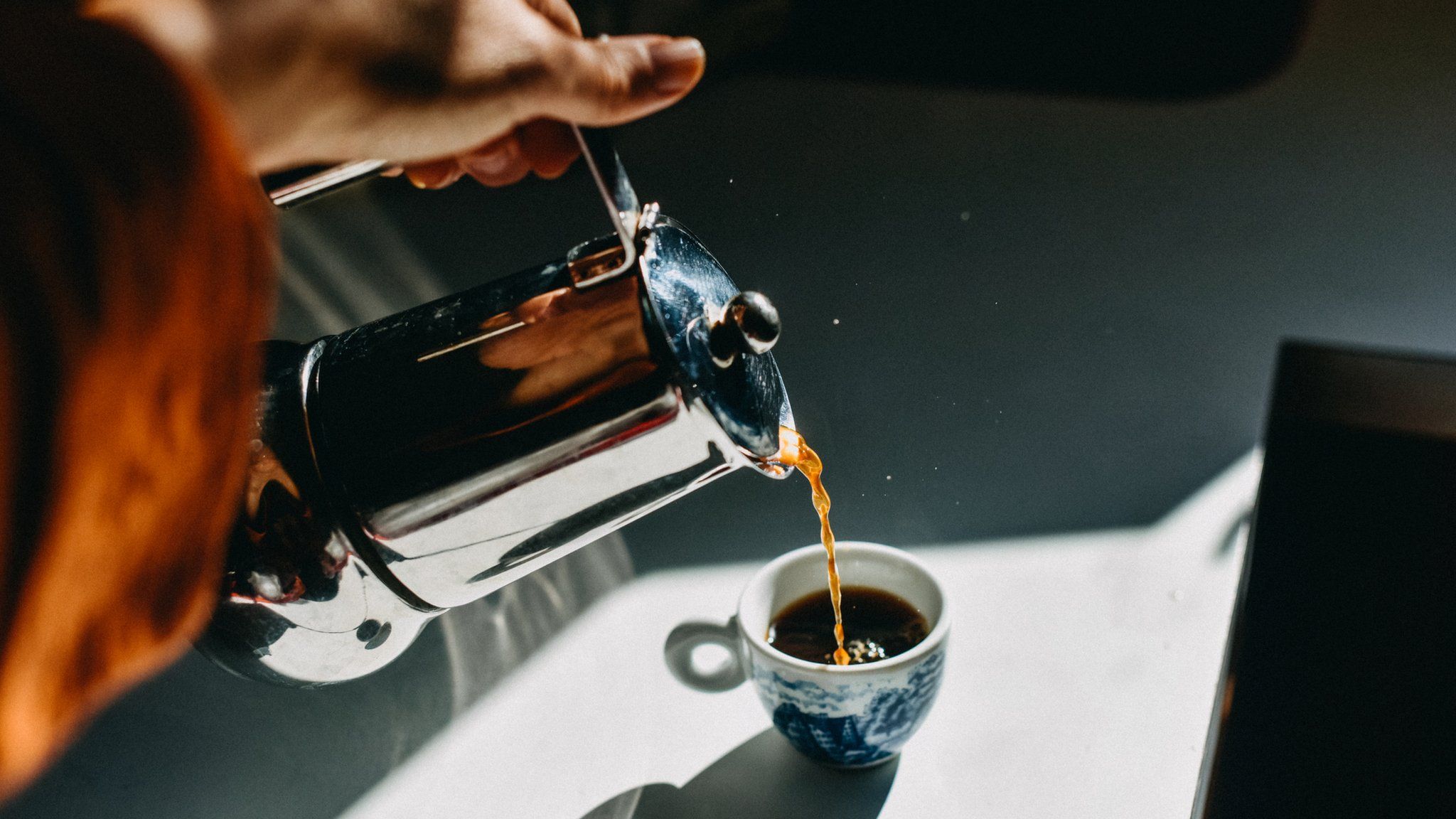 Photo of a woman pouring an espresso cup into a small mug