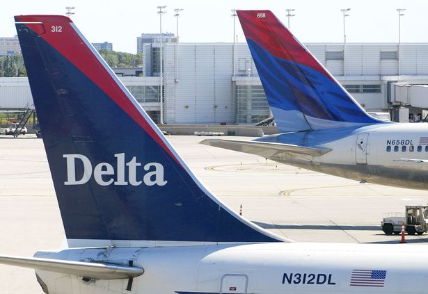 A wing of a Delta airplane with an airport in the background