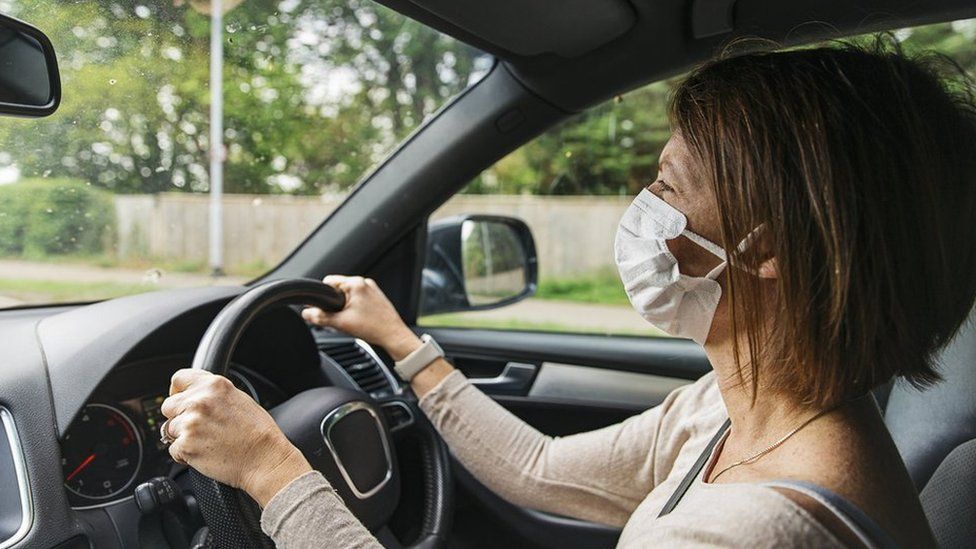 A woman driving a car in a mask