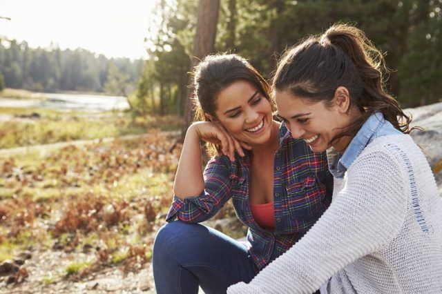 Two women laugh and talk in the countryside. 