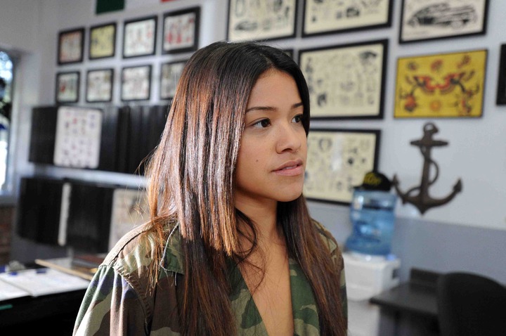 Gina Rodriguez standing in a tattoo shop with flash pieces in frames on the wall in "Filly Brown"