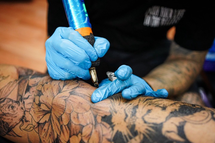 Close-up of a tattoo artist's gloved hands as they tattoo a person's with a black and gray floral design