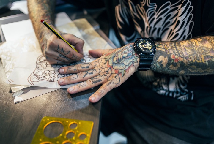 Close-up of a tattoo artist with tattooed arms, drawing on paper with a pencil