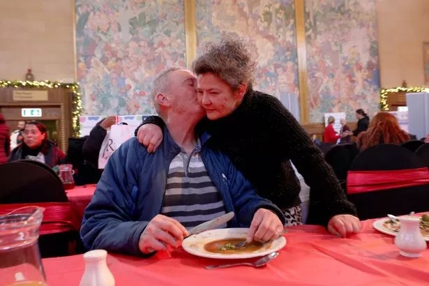 Man sat at table getting a hug from woman